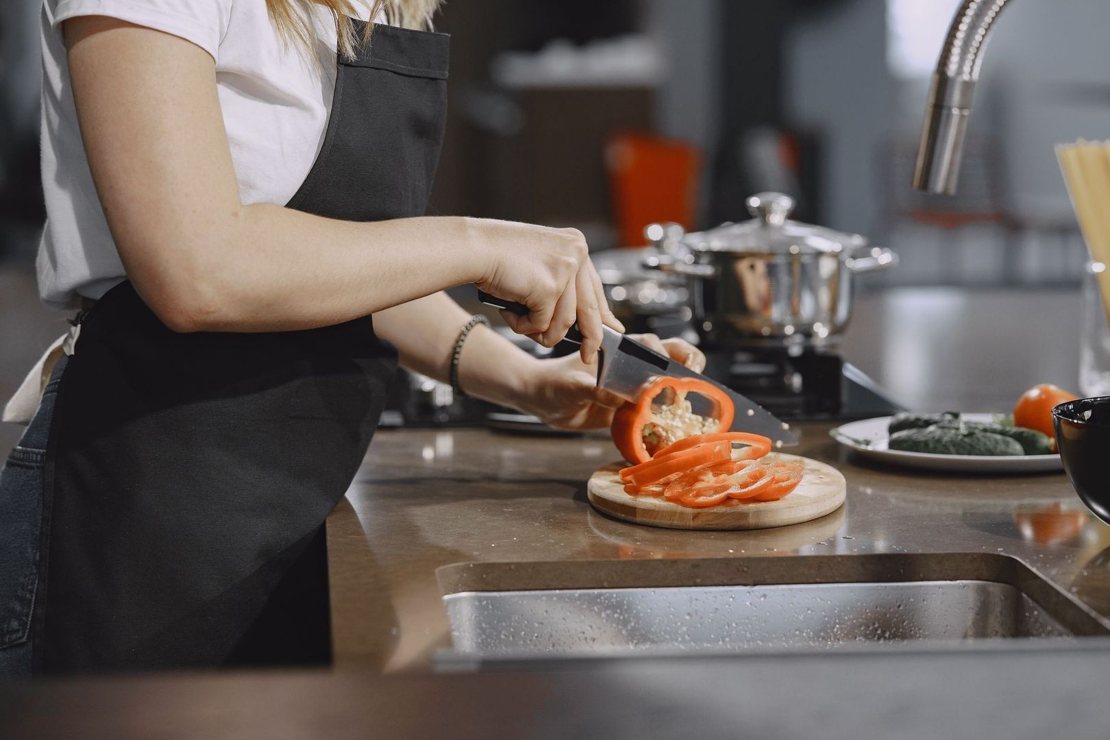 Person i svart förkläde skär paprika vid en välordnad köksstation